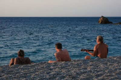 Rear view of people sitting on beach against sky