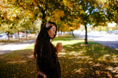 Portrait of young woman standing against trees in autumn