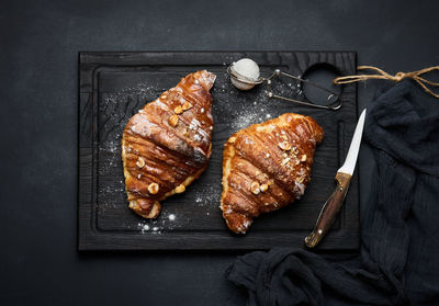 Baked croissant on a wooden board and sprinkled with powdered sugar, black table. appetizing pastrie