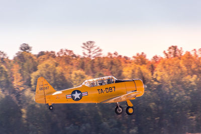 Airplane flying over trees against sky during sunset