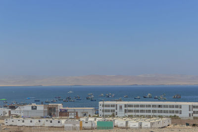 Buildings by sea against clear blue sky