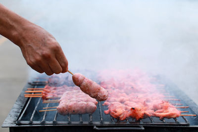 Person holding meat on barbecue grill