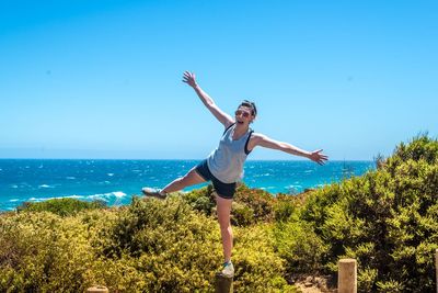 Happy woman balancing on wooden post by plants against sea