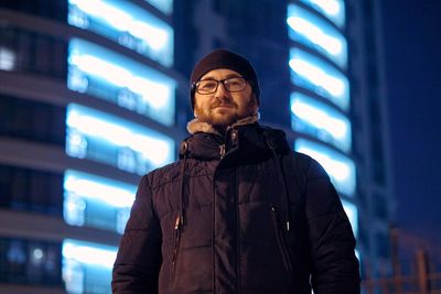 Portrait of man standing in city at night during winter
