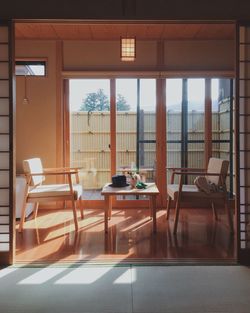 Empty chairs and table by window against sky