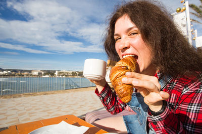 Portrait of woman eating ice cream against sky