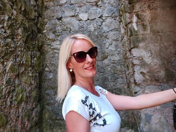 Portrait of young woman wearing sunglasses against wall