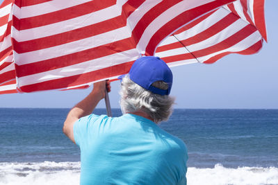 Rear view of senior man holding beach umbrella