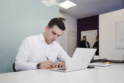 Young businessman writing in front of laptop at desk in office