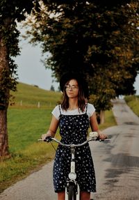 Woman with bicycle standing on footpath against trees