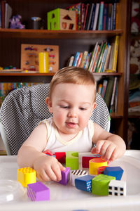 Cute baby boy playing with toy blocks on table