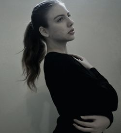 Young woman looking away while standing against wall