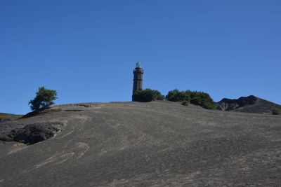 Lighthouse amidst buildings against clear blue sky