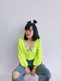 Portrait of young woman sitting against wall