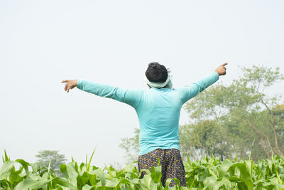 Rear view of man with arms outstretched against clear sky