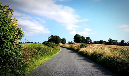 Empty road amidst field against sky