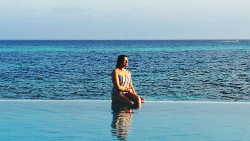 Woman sitting poolside against sea