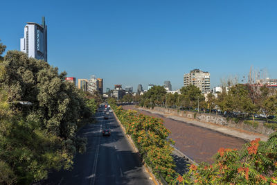 Road amidst buildings against clear blue sky