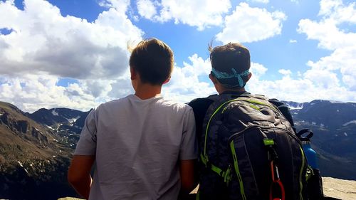 Rear view of friends with backpack standing at observation point against sky