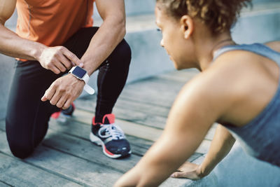 Man using smart watch while female friend doing push ups