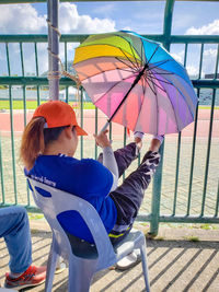 Woman sitting on seat against multi colored umbrella