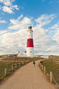 Rear view of boy running on dirt road towards lighthouse against sky