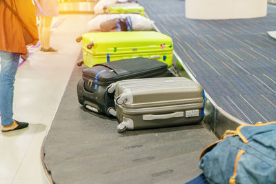 Low section of women standing by suitcases on conveyor belt at airport