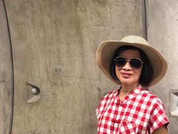 Portrait of smiling woman wearing sunglasses standing against wall