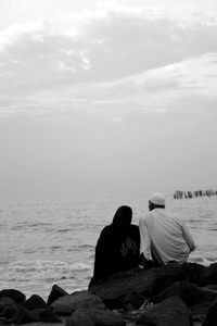 Rear view of people sitting on rock by sea