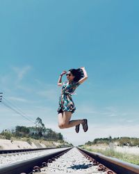 Full length of woman jumping on railroad track against sky