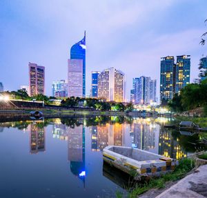 Illuminated buildings by lake against blue sky