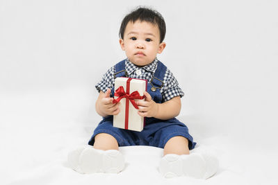 Portrait of cute baby boy playing with toy against white background
