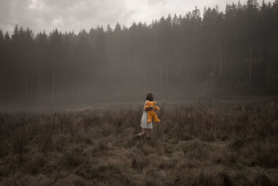Side view of woman with teddy bear walking on grassy field against trees in forest