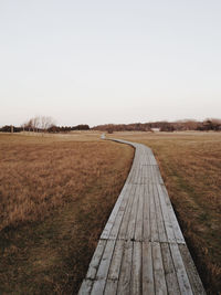 Empty boardwalk on grassy field against clear sky