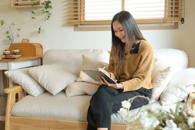 Young woman using digital tablet while sitting on sofa at home
