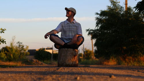 Man sitting on log over road against sky