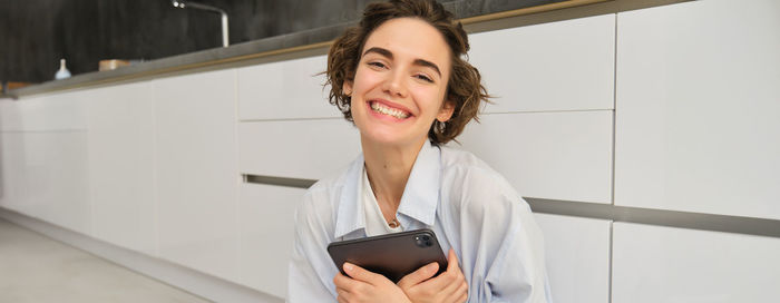 Portrait of young woman using mobile phone while standing in office