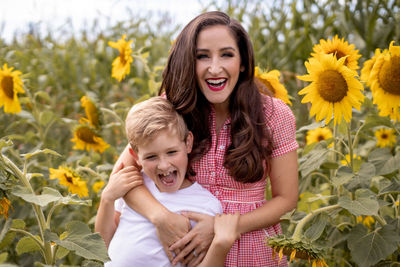 Portrait of happy mother and son standing against sunflowers