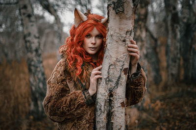 Portrait of woman standing by tree trunk in forest