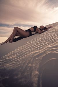 Side view of seductive woman lying on desert against sky