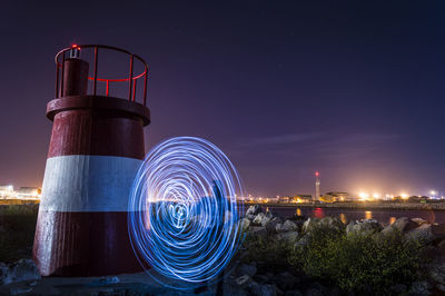 Person light painting by lookout tower against sky at night