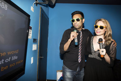 Happy couple singing karaoke while standing in nightclub
