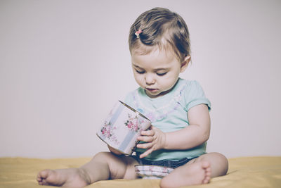 Cute baby girl playing with box on bed at home