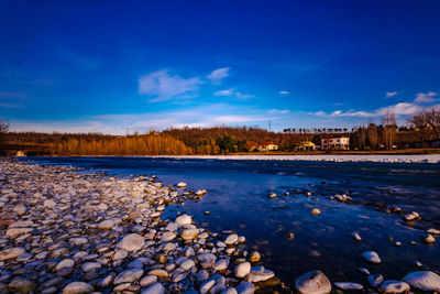 Surface level of stones by calm lake against blue sky