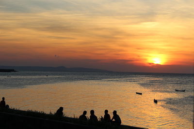 Silhouette people on beach against sky during sunset