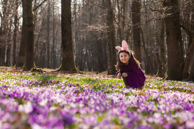 Portrait of smiling woman sitting by purple flowers in forest