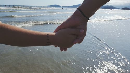 Cropped image of father and child holding hands at beach