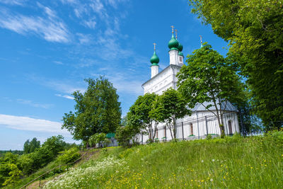 A snow-white church with green domes on the edge of a high cliff on a sunny summer day.