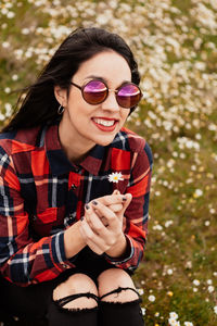 Portrait of smiling woman holding flower while sitting on field