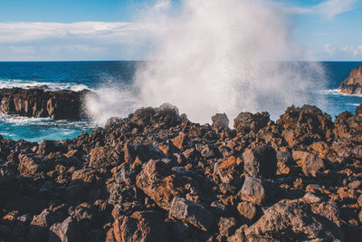 Waves splashing on rocks at shore against sky